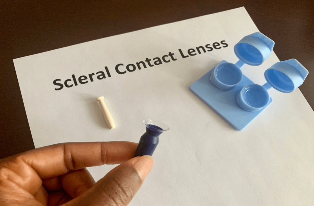 A person using a tool to insert scleral contact lenses into the eye, with a contact lens case next to it
