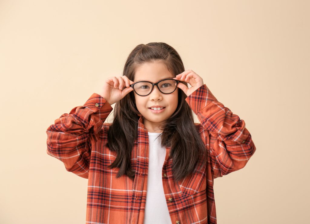 A young girl wearing eye glasses due to myopia, holding onto the edge of her glasses while smiling