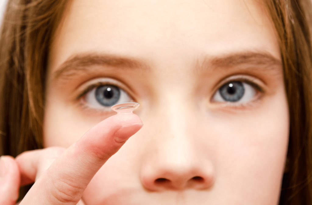 A young girl holds a MiSight contact lens on her index finger close to her face