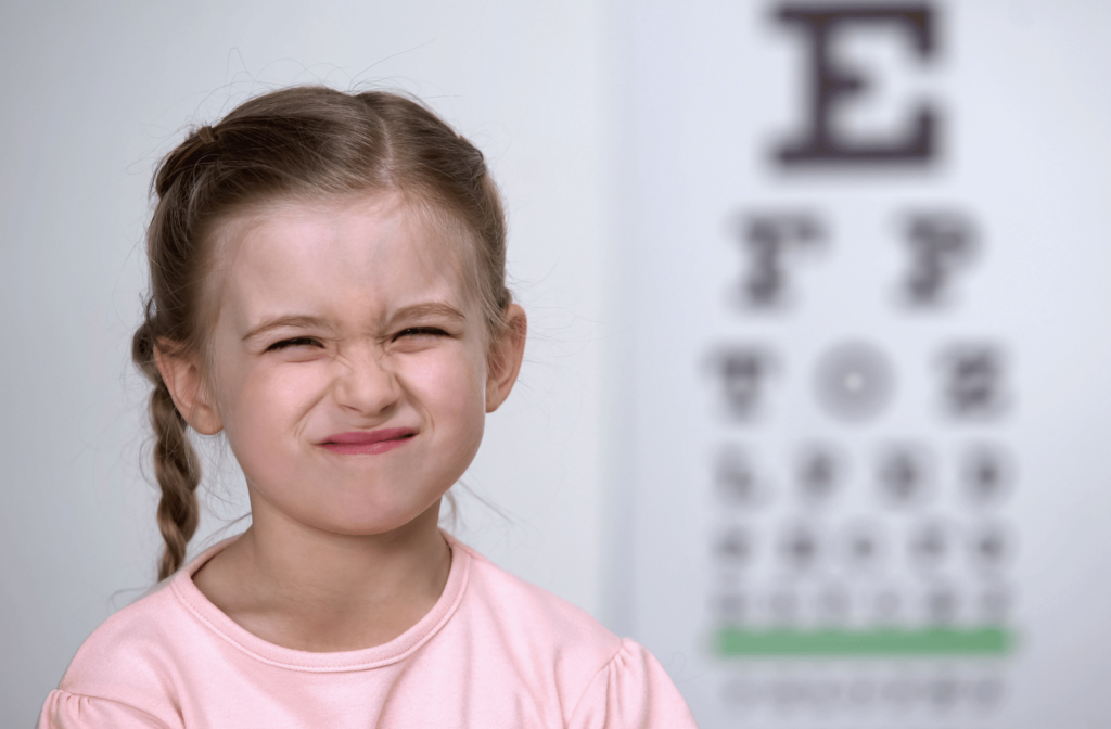 A girl is squinting her eyes trying to see letters on the chart for a vision test