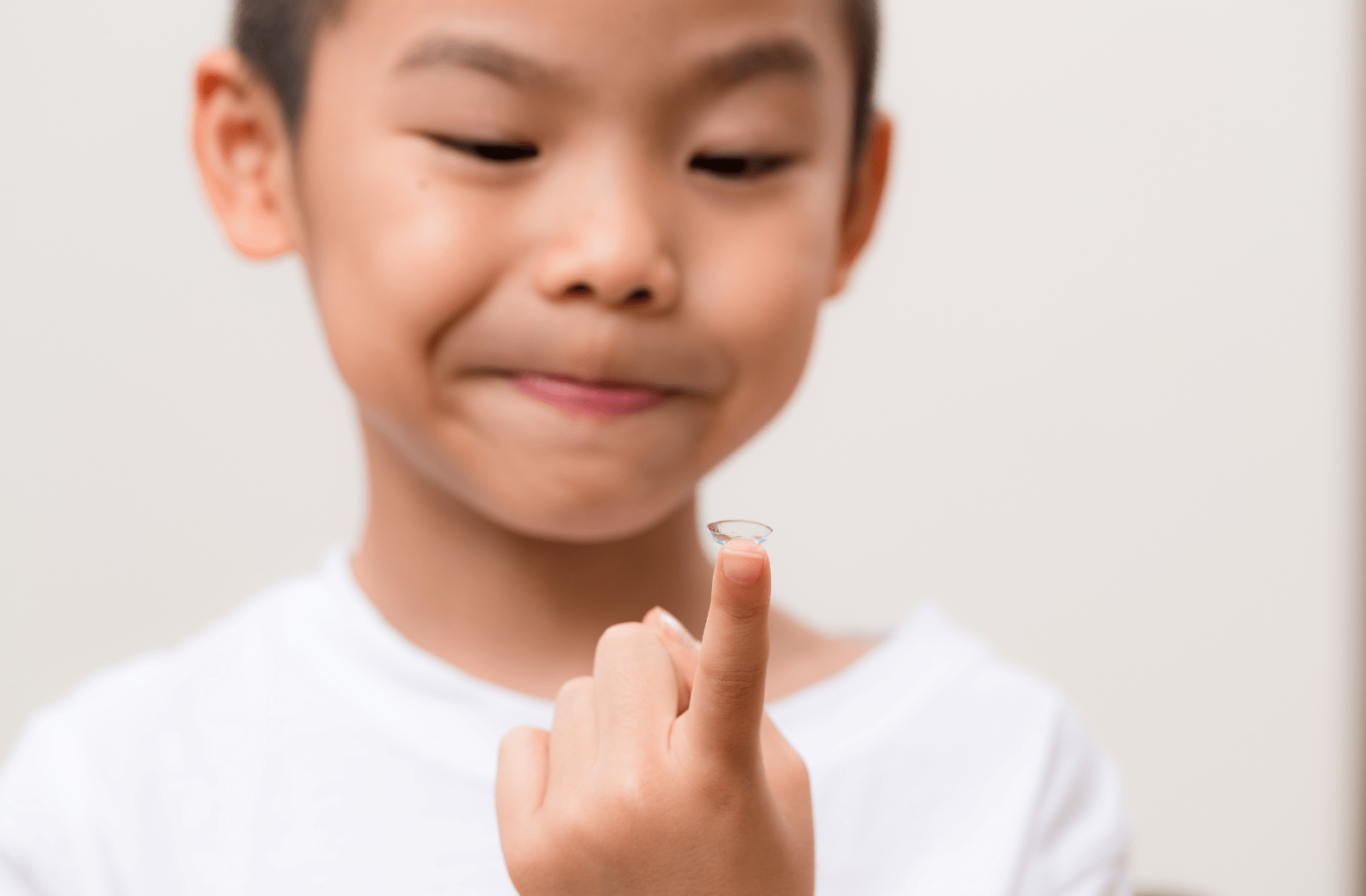 A boy in a white shirt holding a contact lens on the tip of his index finger