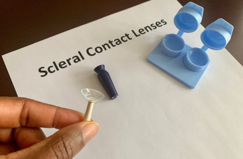 A human hand is holding a contact lens insertion device with a scleral contact lens