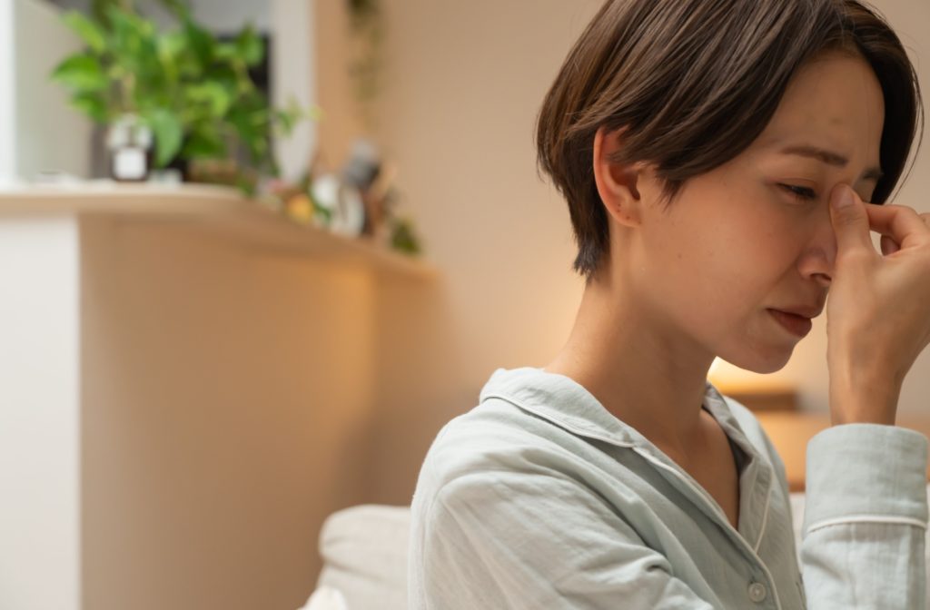 An adult experiencing dry eye discomfort and a headache attempts to find relief by pinching the bridge of their nose.