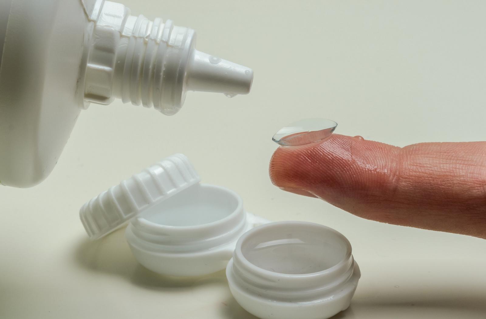 Contact lens resting on a fingertip beside a lens case and solution, representing non-surgical keratoconus treatment options.